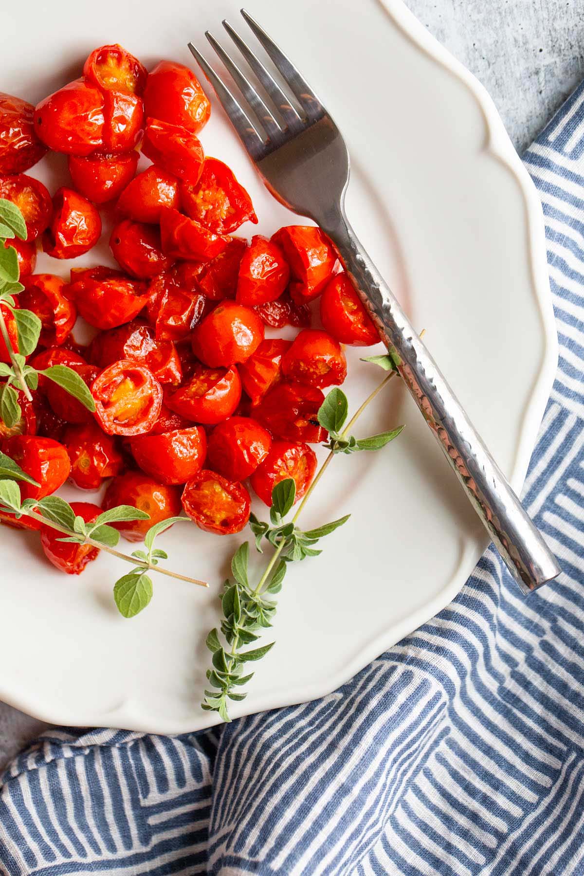 Harissa Roasted Cherry Tomatoes on a white plate with fresh herbs.