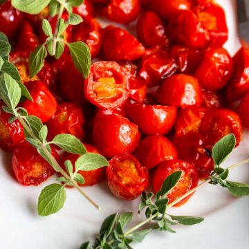 Harissa Roasted Tomatoes on a white plate with fresh herbs.