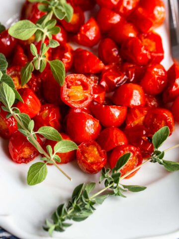 Harissa Roasted Tomatoes on a white plate with fresh herbs.