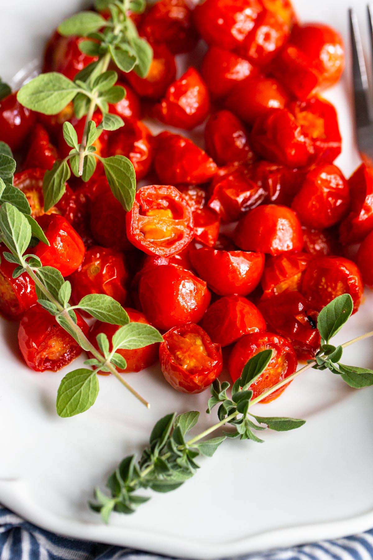 Harissa Roasted Tomatoes on a white plate with fresh herbs.