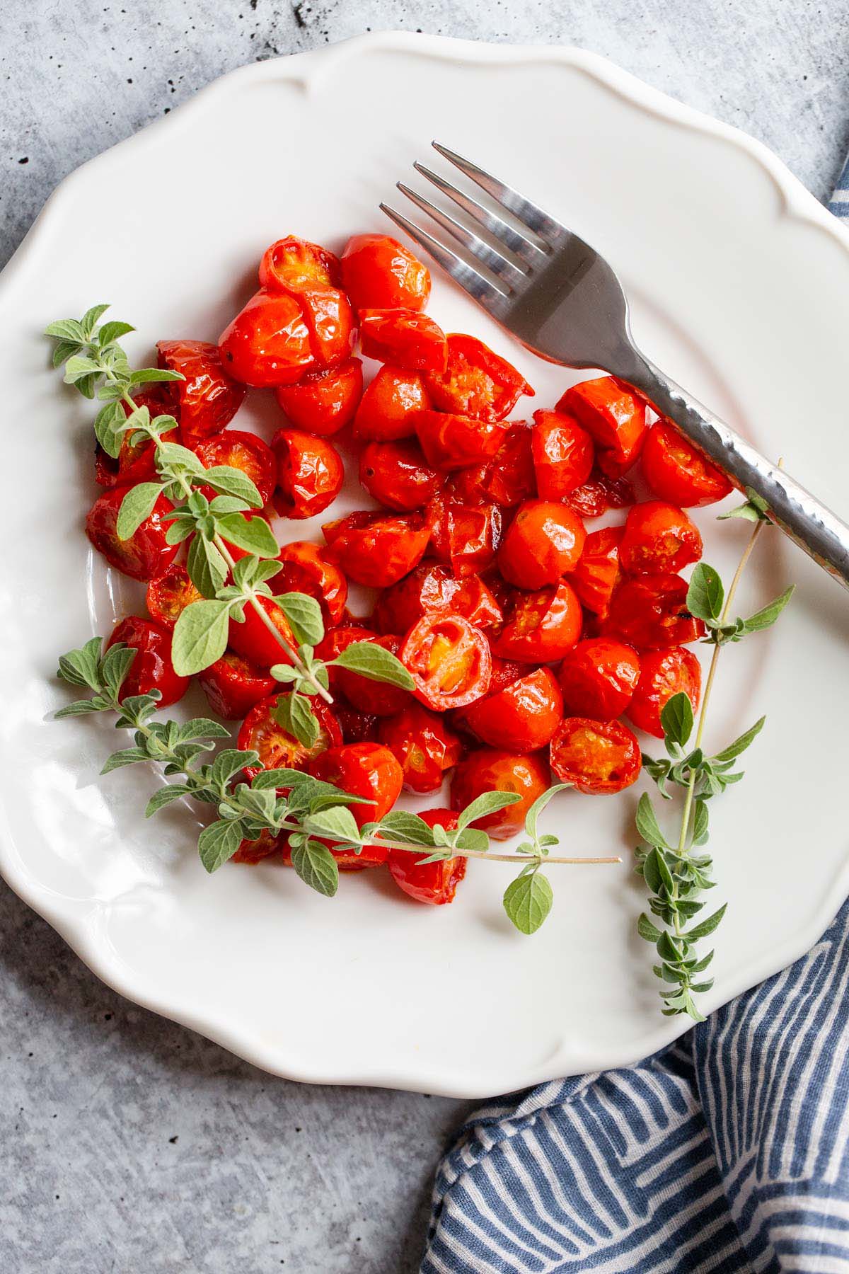 Harissa Roasted Tomatoes on a white plate with fresh herbs.