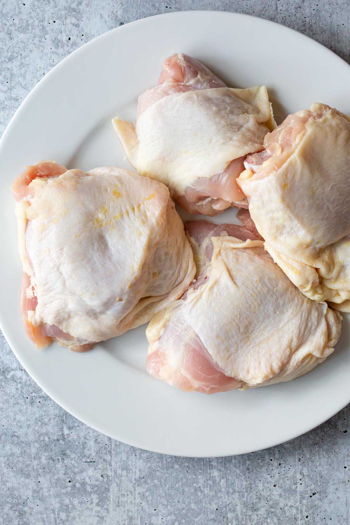 Raw chicken thighs on a white plate.