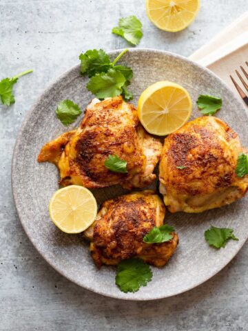 Cooked chicken thighs with lemon slices and fresh herbs.