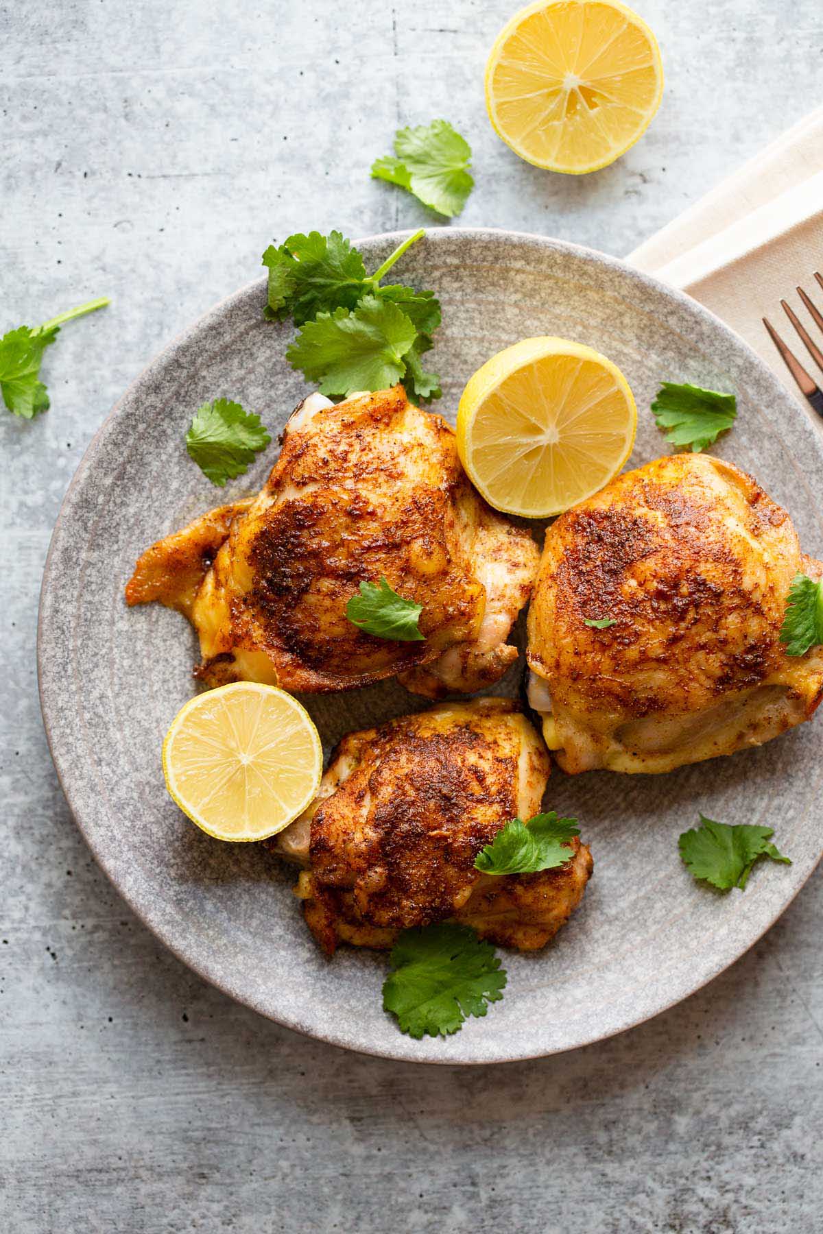 Cooked chicken thighs with lemon slices and fresh herbs.