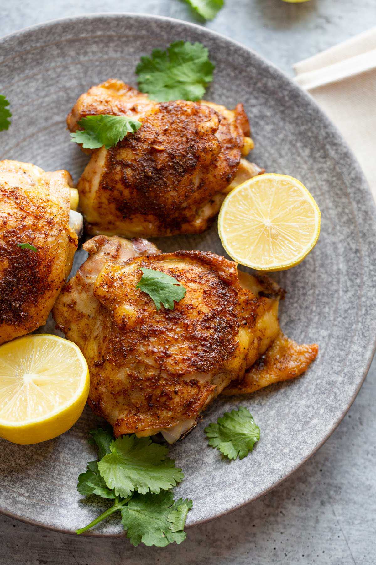 Cooked chicken thighs with lemon slices and fresh herbs.