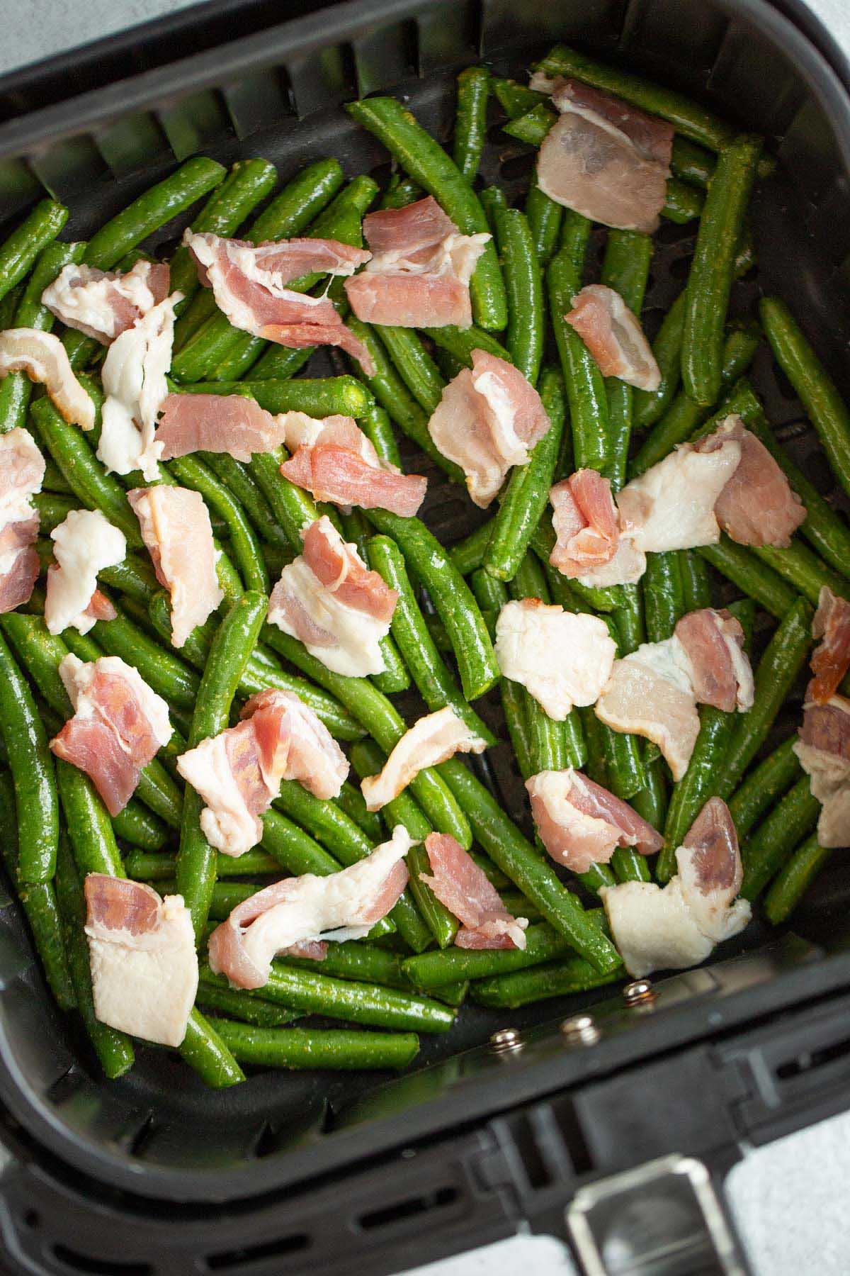 Uncooked green beans and bacon in air fryer.