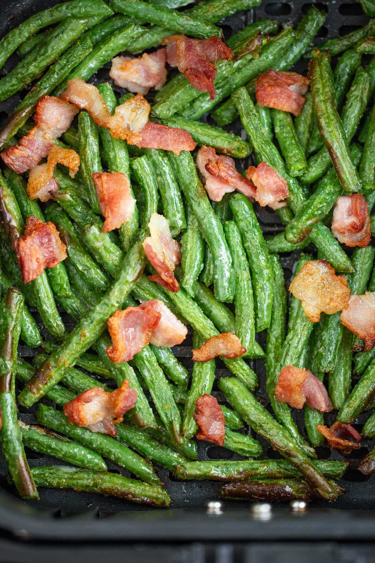 Cooked green beans and bacon in air fryer basket.