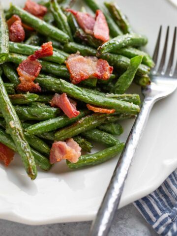 Green beans and bacon on a white plate.