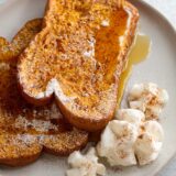 Pumpkin French toast on a plate with whipped cream and syrup.