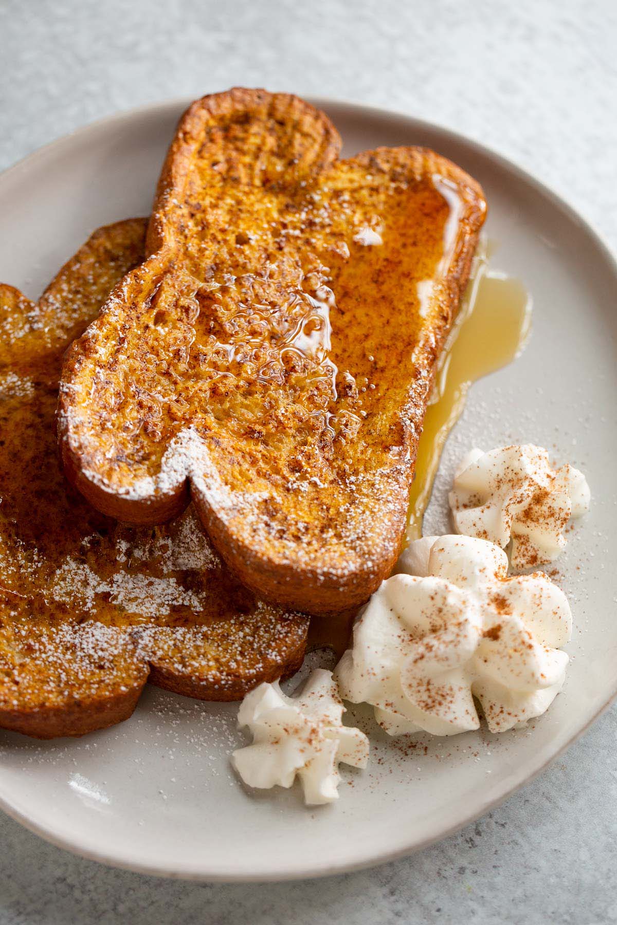 Pumpkin French toast on a plate with whipped cream and syrup.