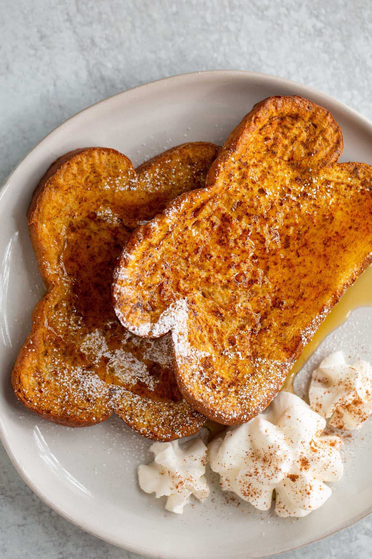 Pumpkin French toast on a plate with whipped cream and syrup.