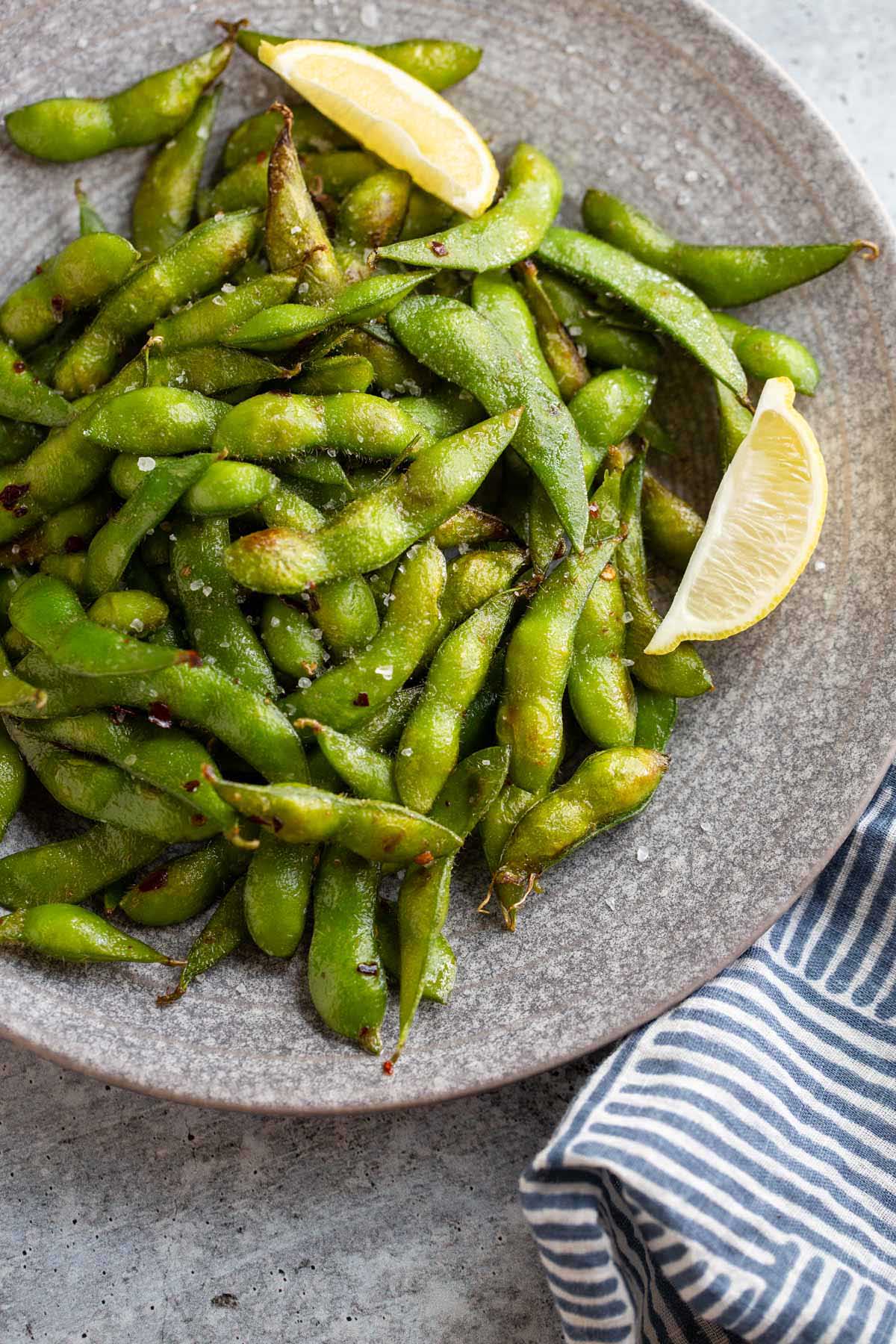 Cooked edamame on a plate with lemon wedges.