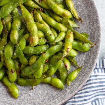 Cooked edamame on a plate with lemon wedges.