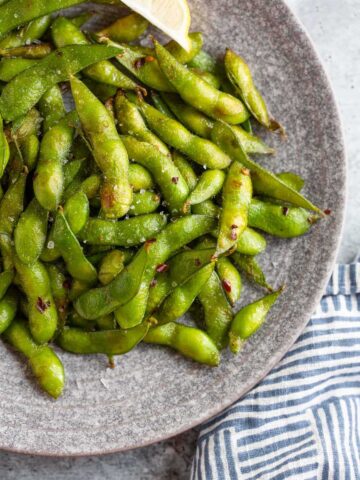 Cooked edamame on a plate with lemon wedges.