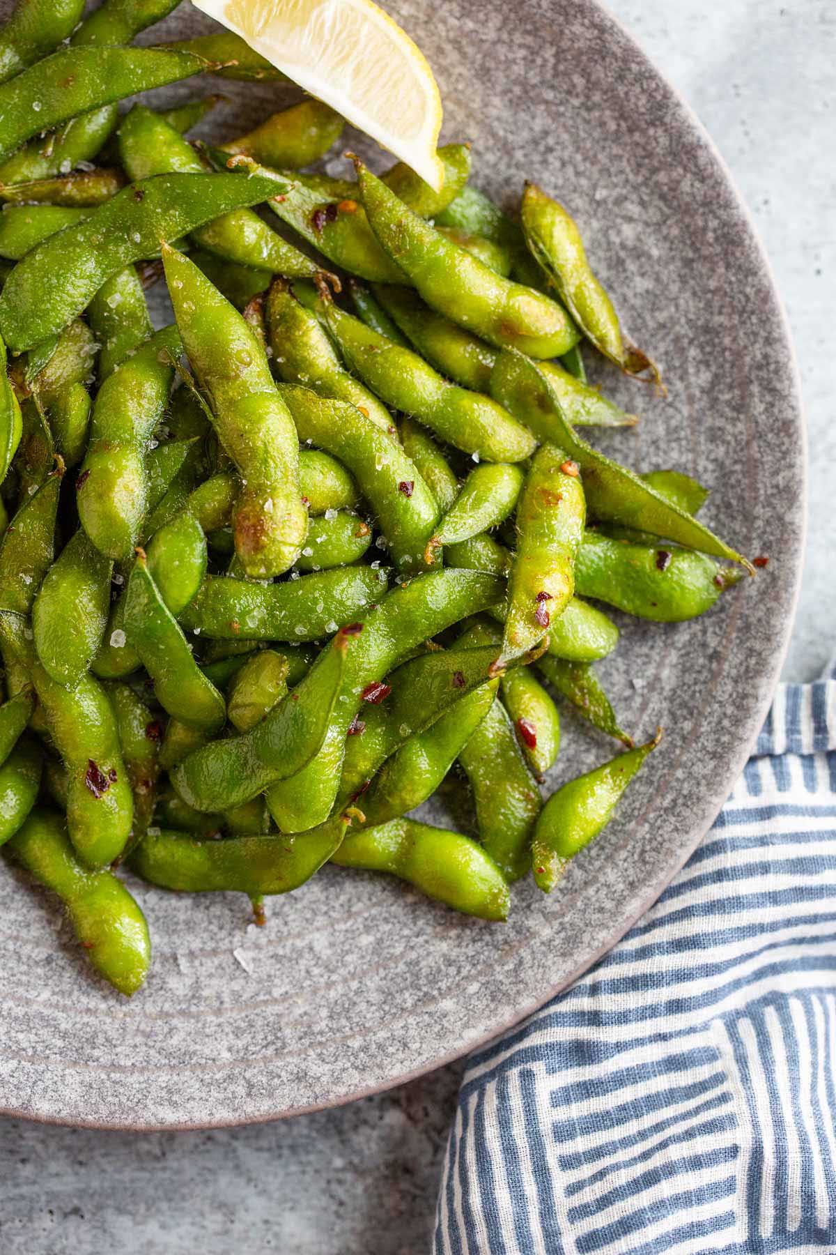 Cooked edamame on a plate with lemon wedges.