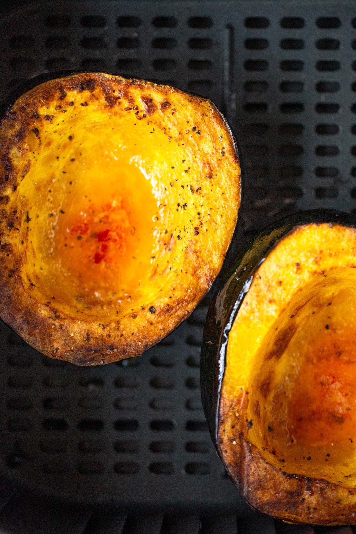 Cooked acorn squash halves in air fryer basket.