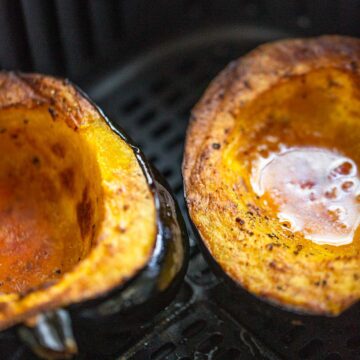 Cooked acorn squash halves in air fryer basket.