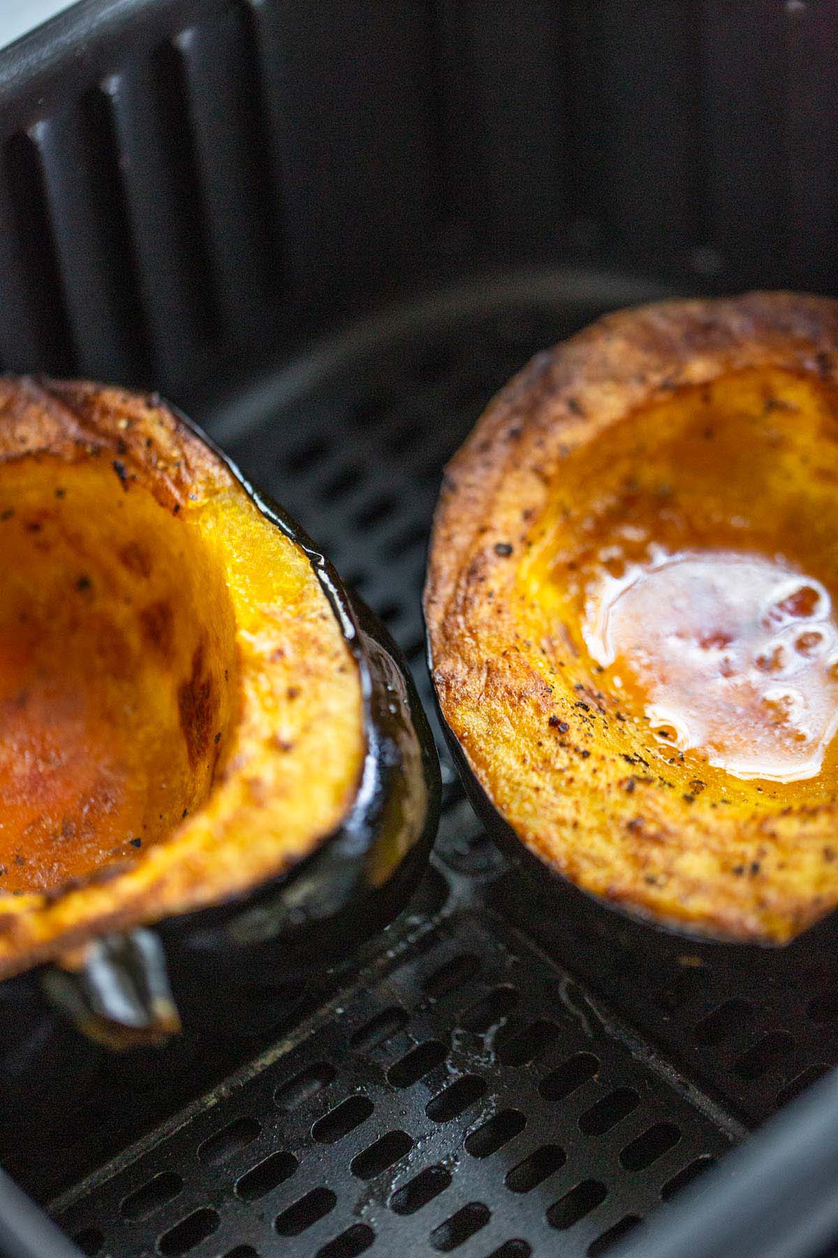 Cooked acorn squash halves in air fryer basket.