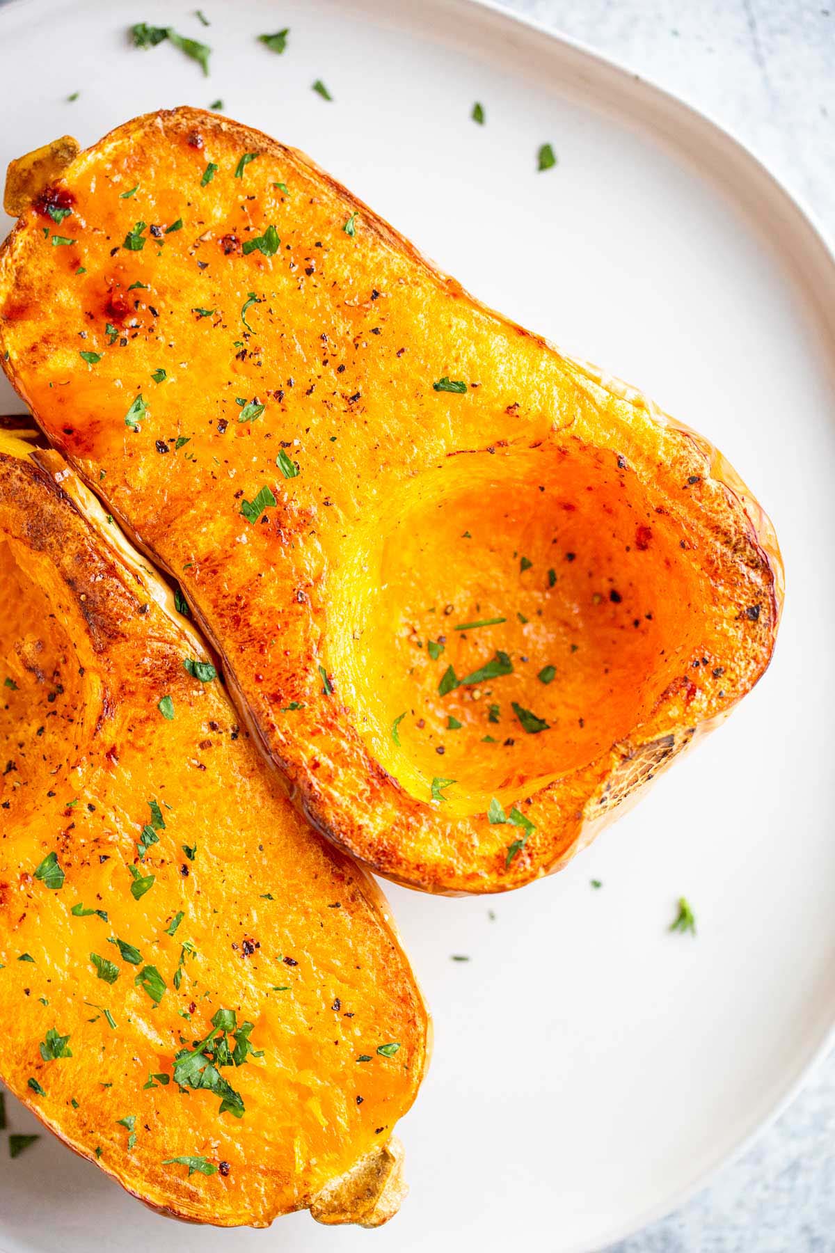 Butternut squash halves on a plate with chopped parsley.