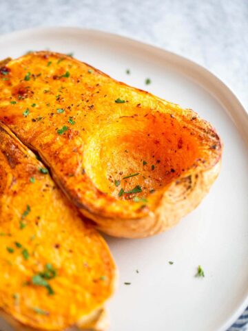 Butternut squash halves on a plate with chopped parsley.