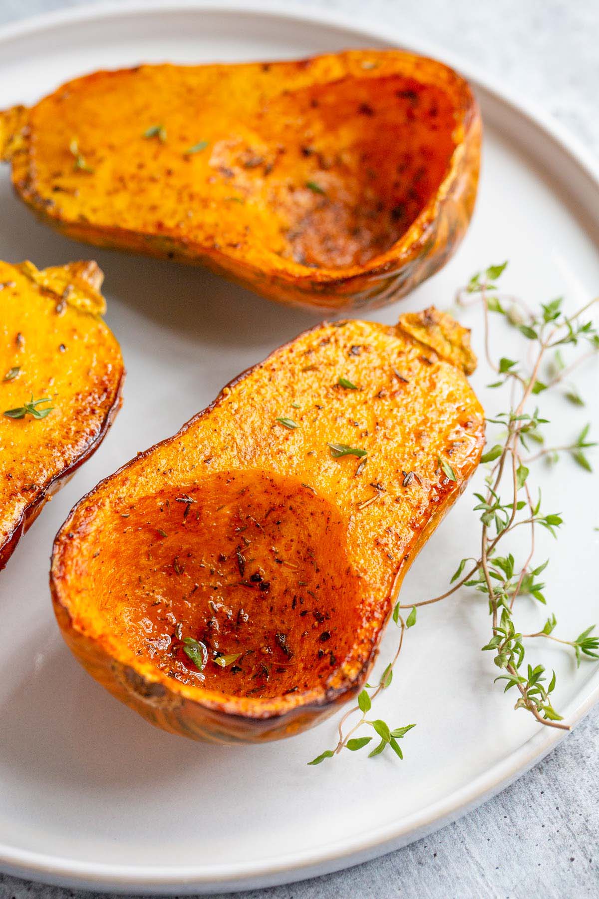 Roasted honeynut squash on a plate with thyme leaves.