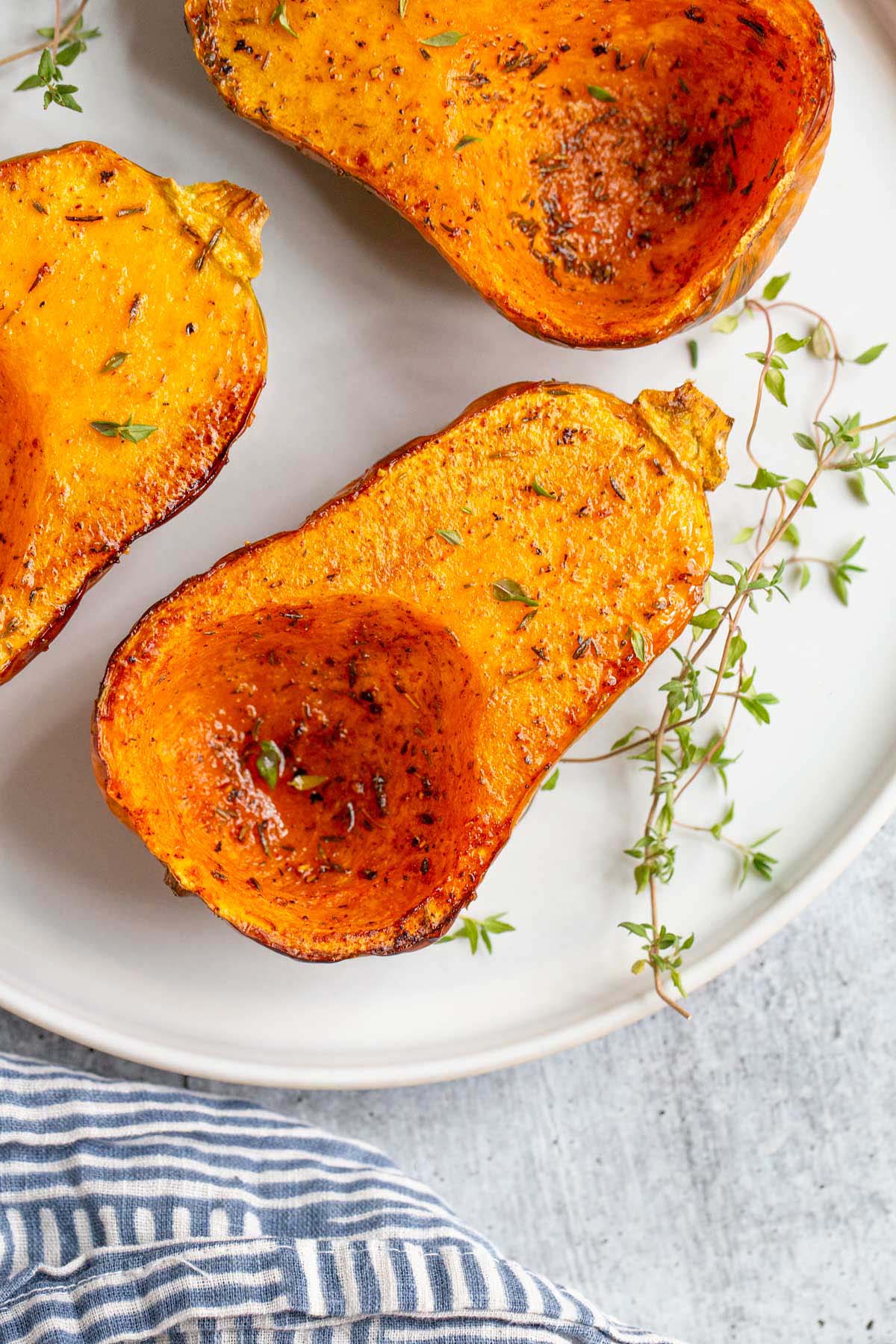 Roasted honeynut squash on a plate with thyme leaves.