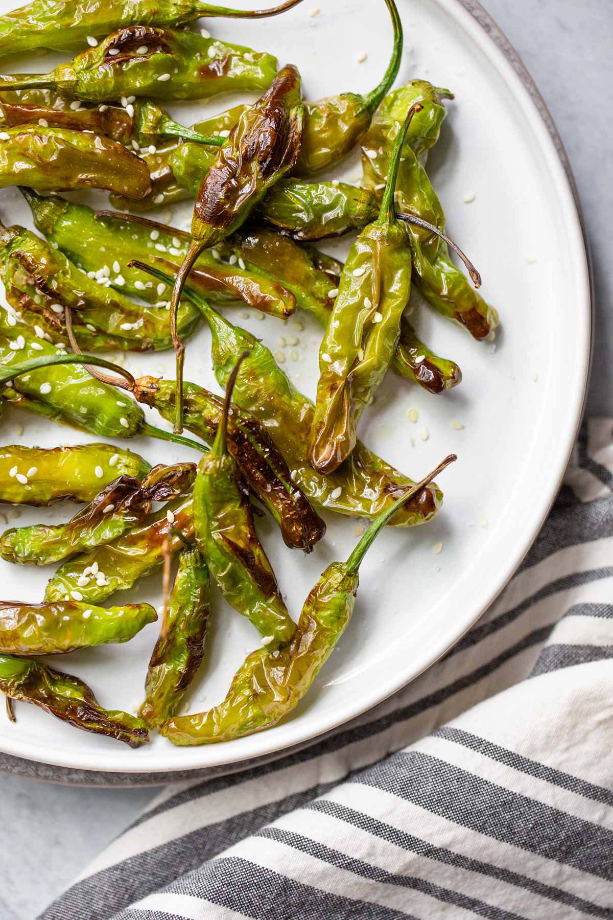 Air fried shishito peppers on a plate with sesame seeds.