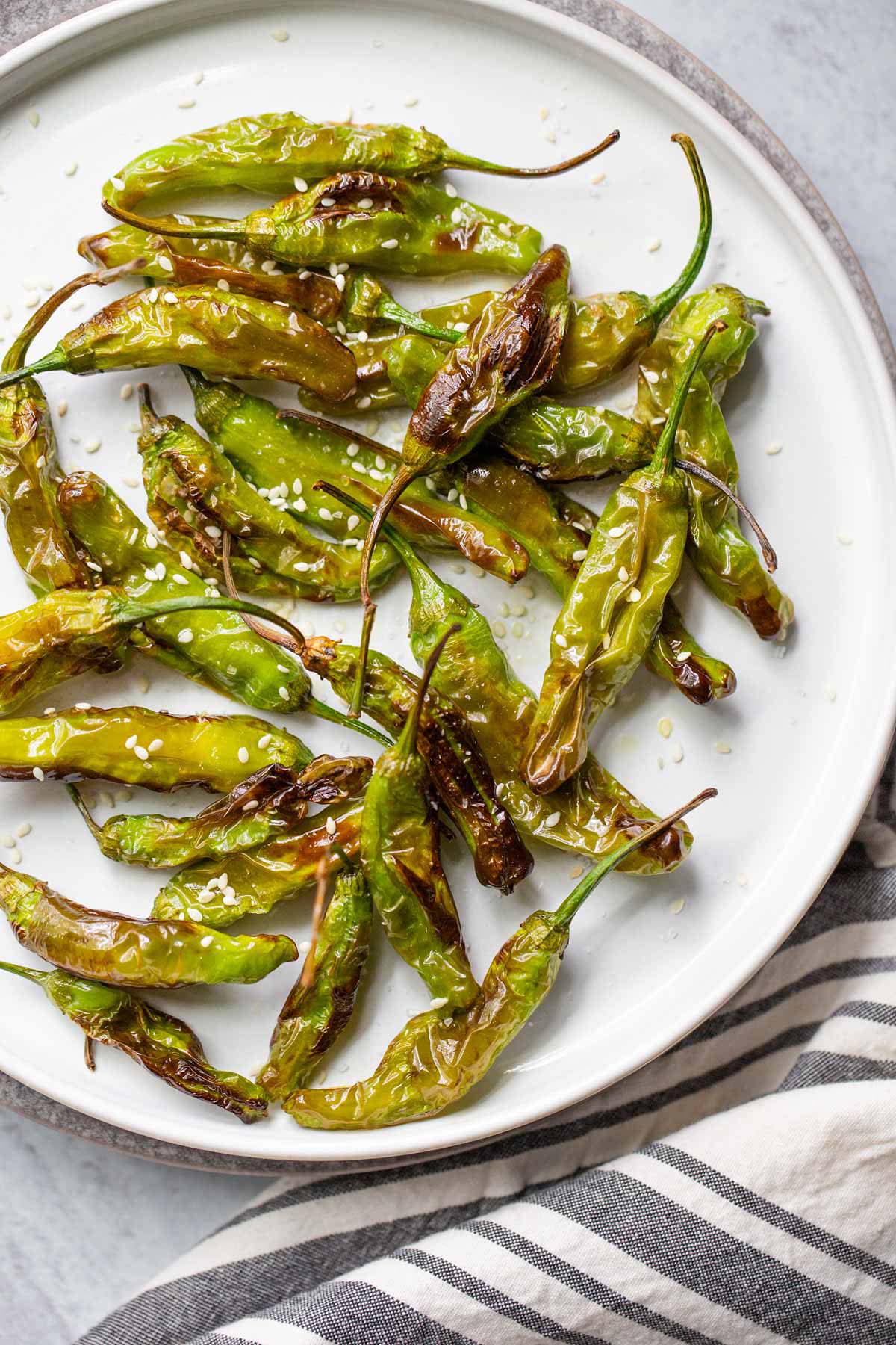 Air fried shishito peppers on a plate with sesame seeds.