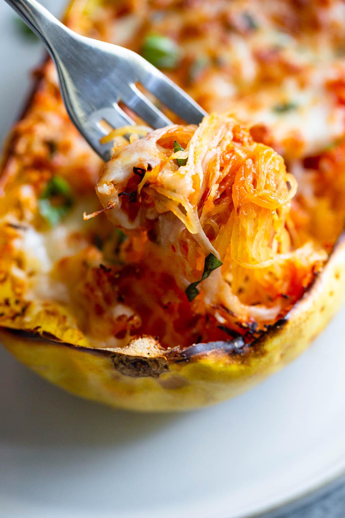 Cheesy spaghetti squash boat on a white plate with a fork.