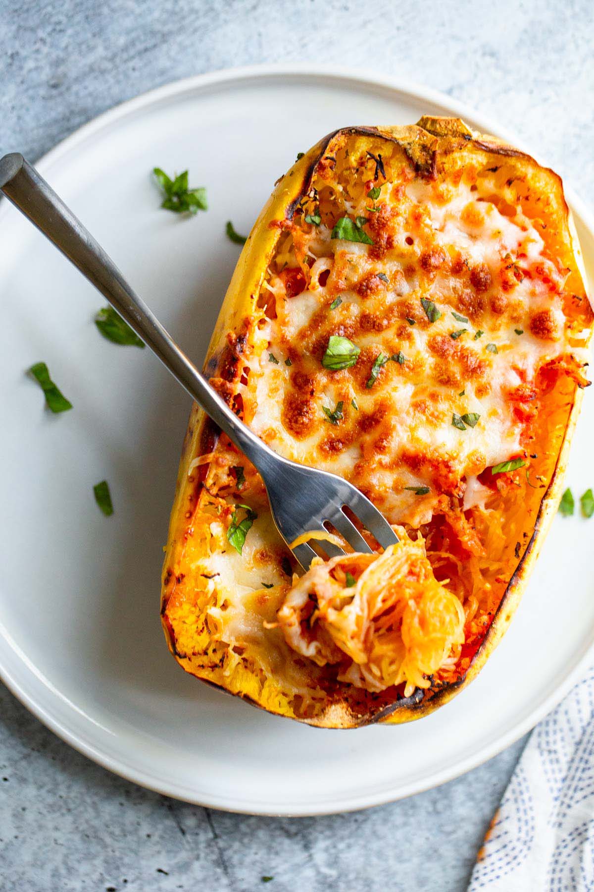 Cheesy spaghetti squash boat on a white plate with a fork.