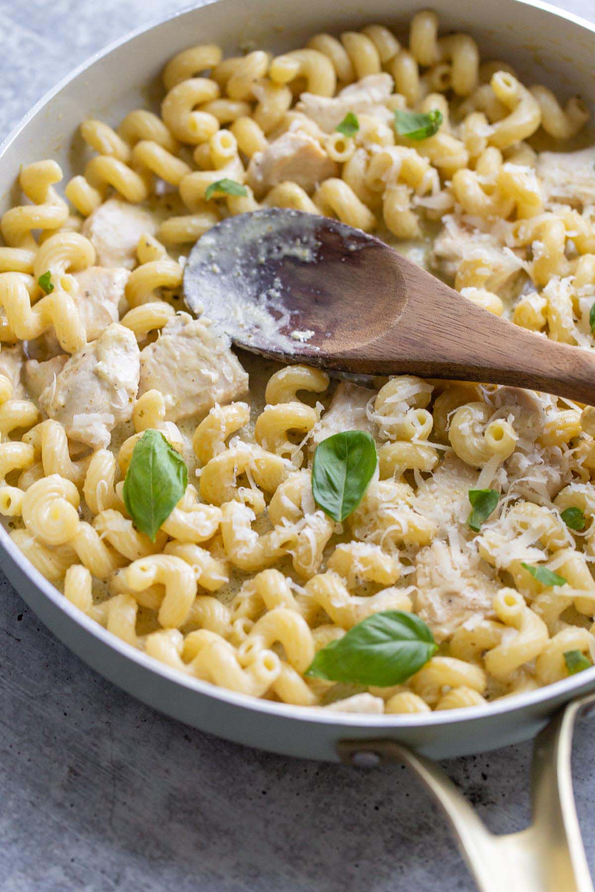 Creamy pesto cavatappi in a skillet with a wooden spoon.