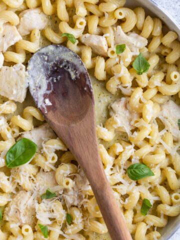 Creamy pesto cavatappi in a skillet with a wooden spoon.