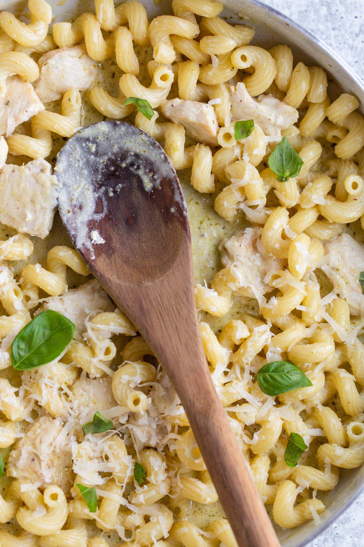 Creamy pesto cavatappi in a skillet with a wooden spoon.