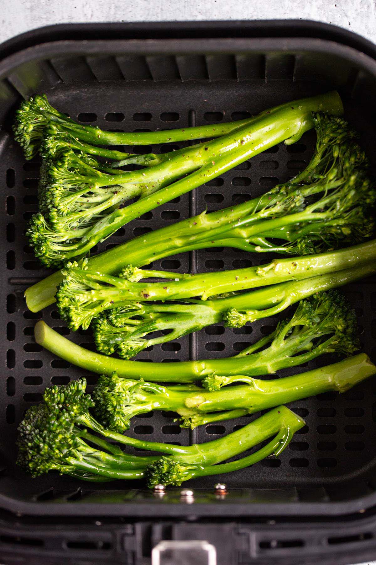 Raw broccolini in air fryer basket.