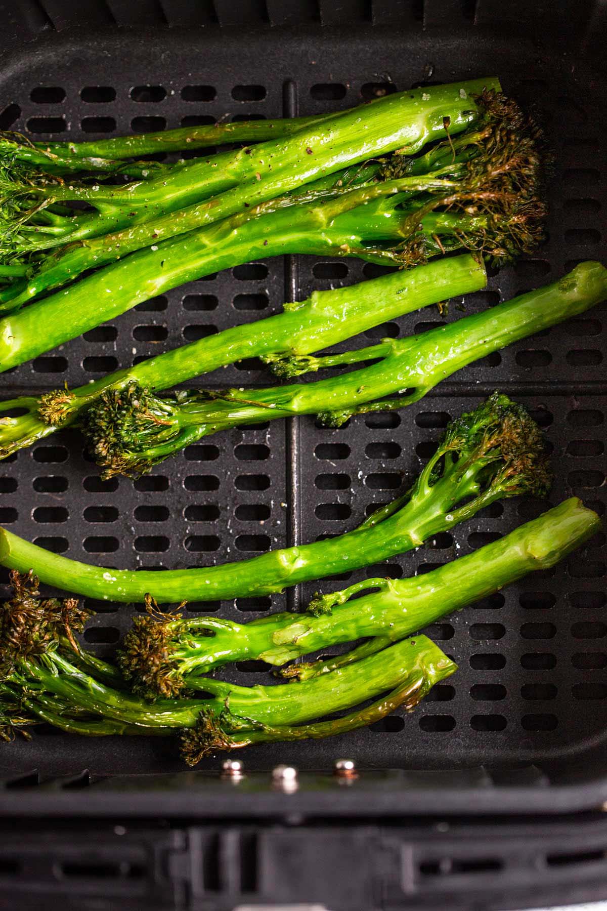 Cooked broccolini in air fryer basket.