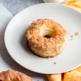 Donut on a plate with a glass of milk in the background.