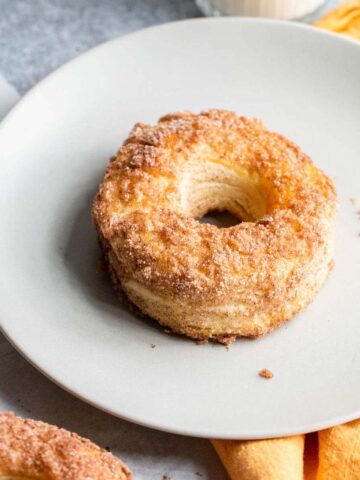 Donut on a plate with a glass of milk in the background.