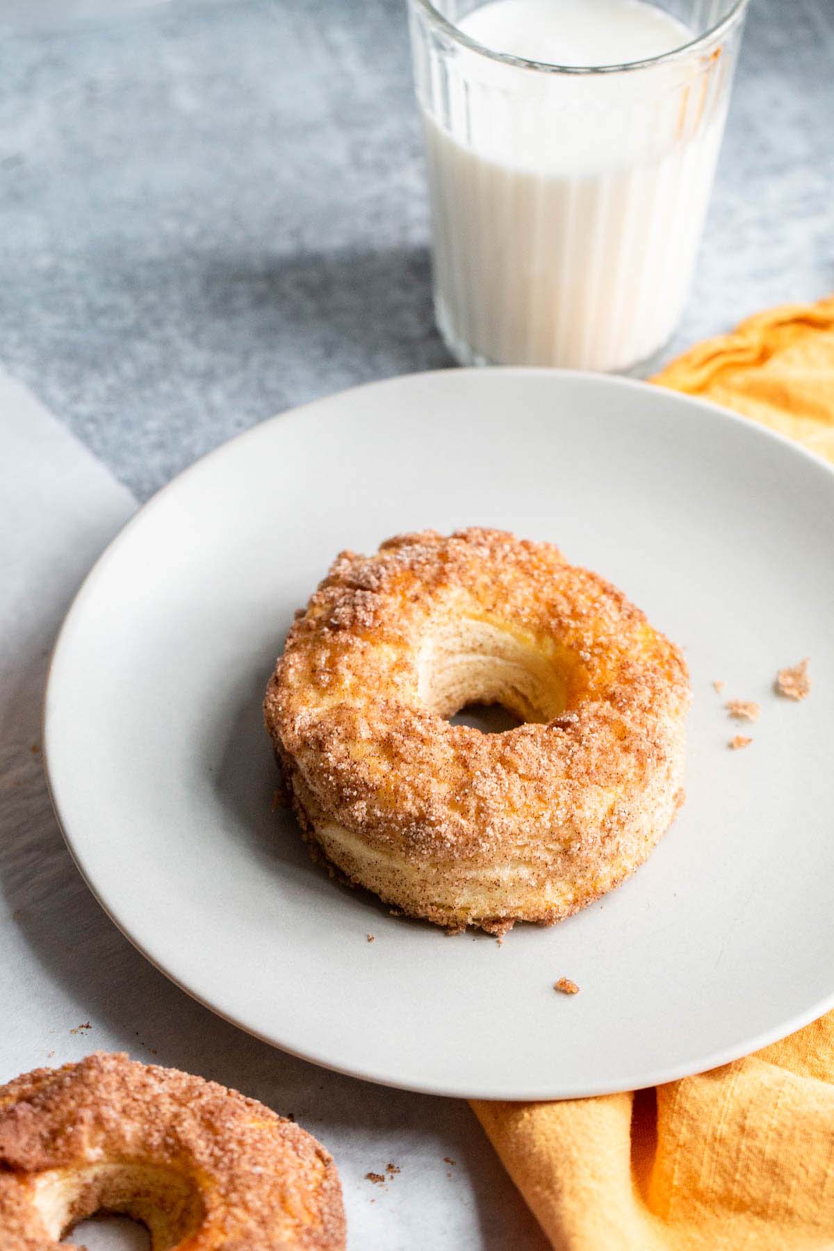 Donut on a plate with a glass of milk in the background.