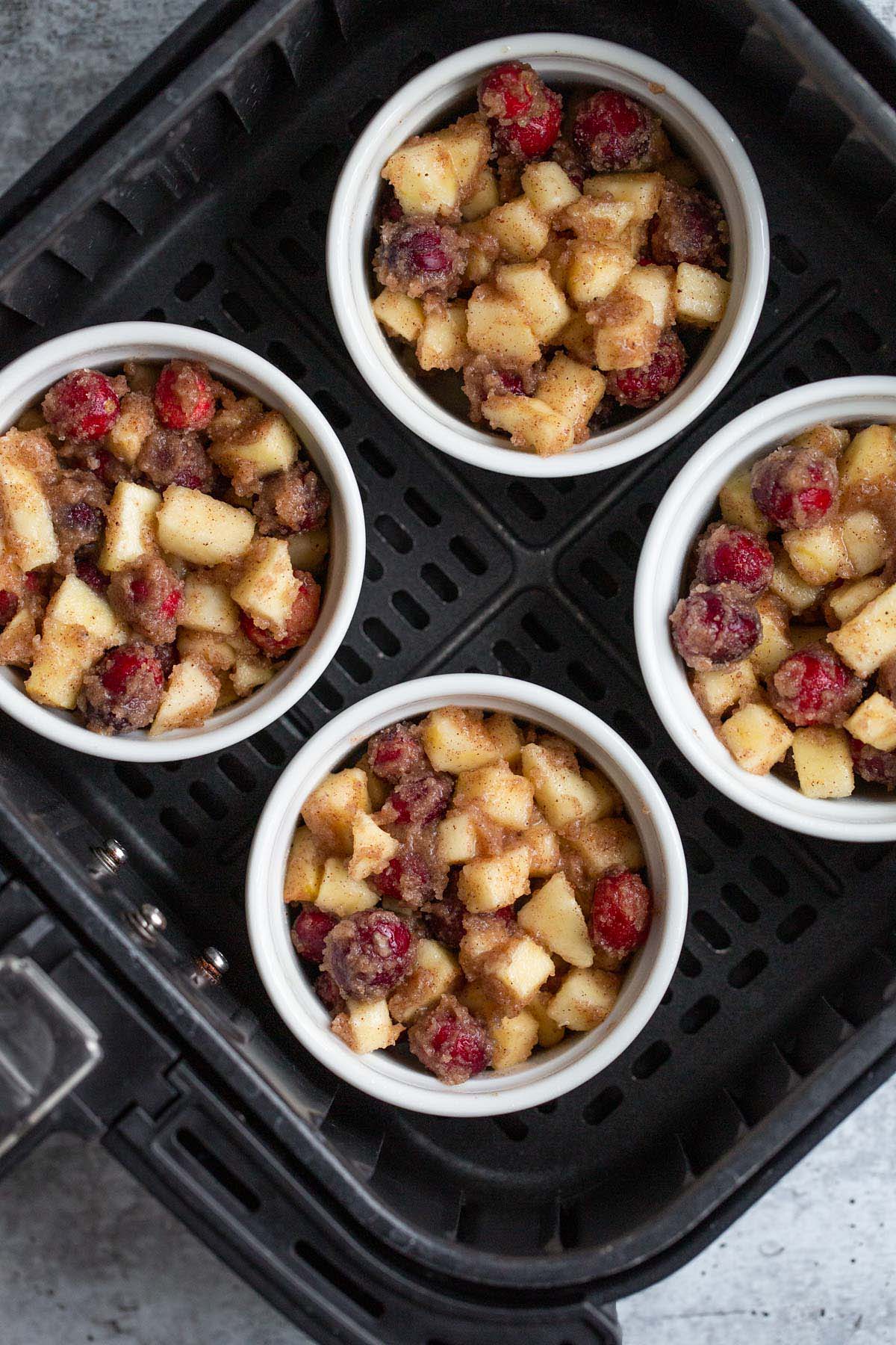 Uncooked apple cranberry crumbles in air fryer basket.