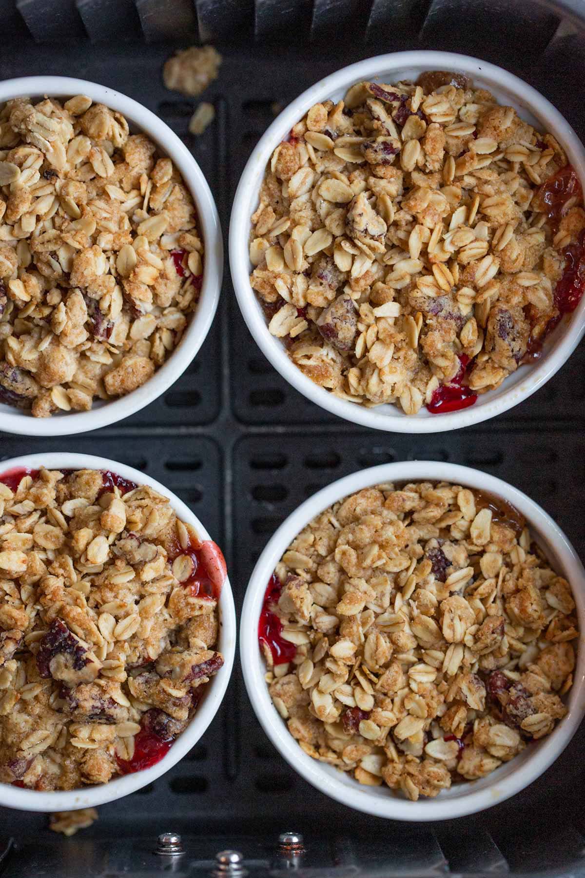 Cooked cranberry apple crumbles in ramekins in the air fryer basket.