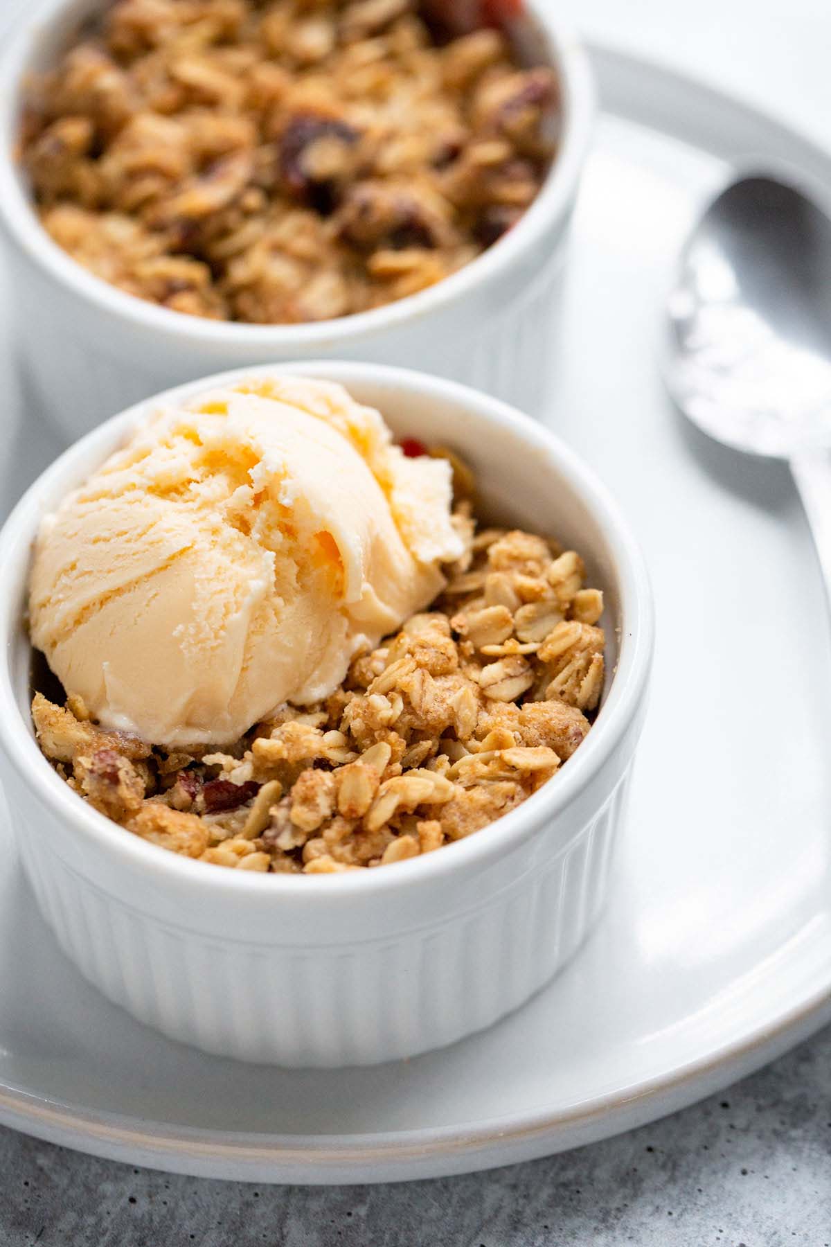 Two apple cranberry crumbles in ramekins with a scoop of vanilla ice cream on one.