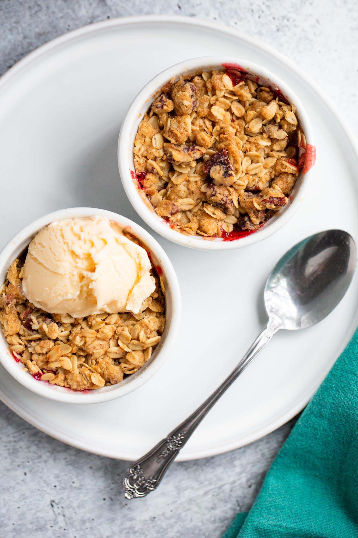 Two apple cranberry crumbles in ramekins with a scoop of vanilla ice cream on one.