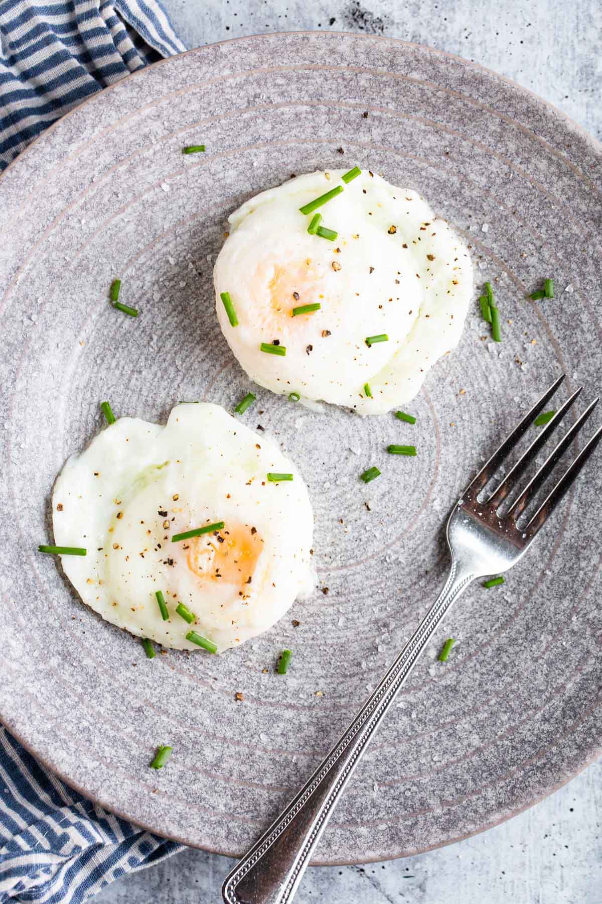 Two poached eggs on a grey plate with chives.