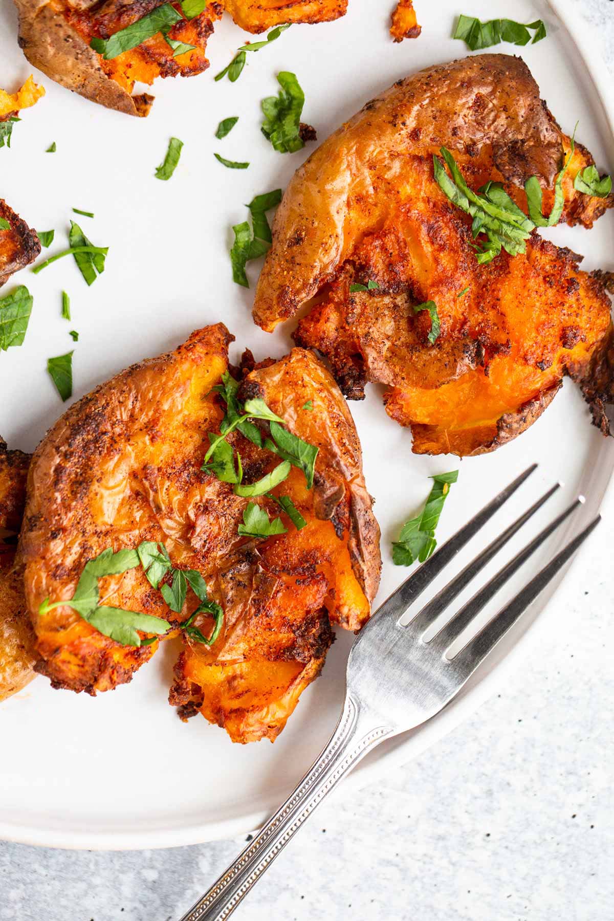 Smashed potatoes on a white plate topped with chopped parsley.