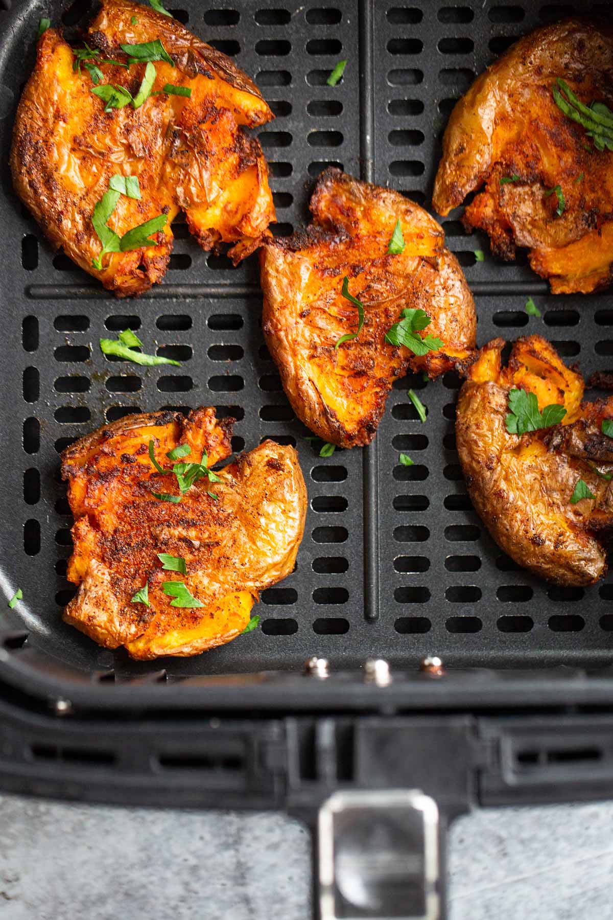 Cooked smashed potatoes in an air fryer basket.