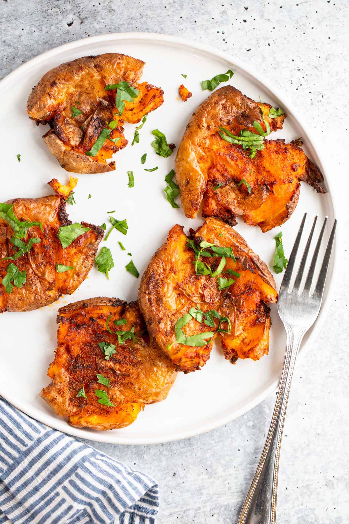 Smashed potatoes on a white plate topped with chopped parsley.