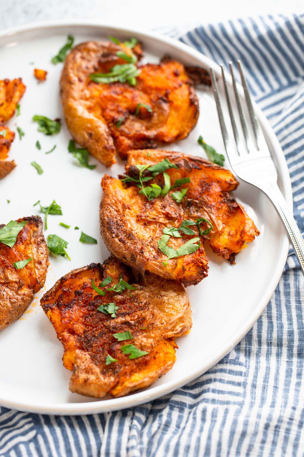 Smashed potatoes on a white plate topped with chopped parsley.