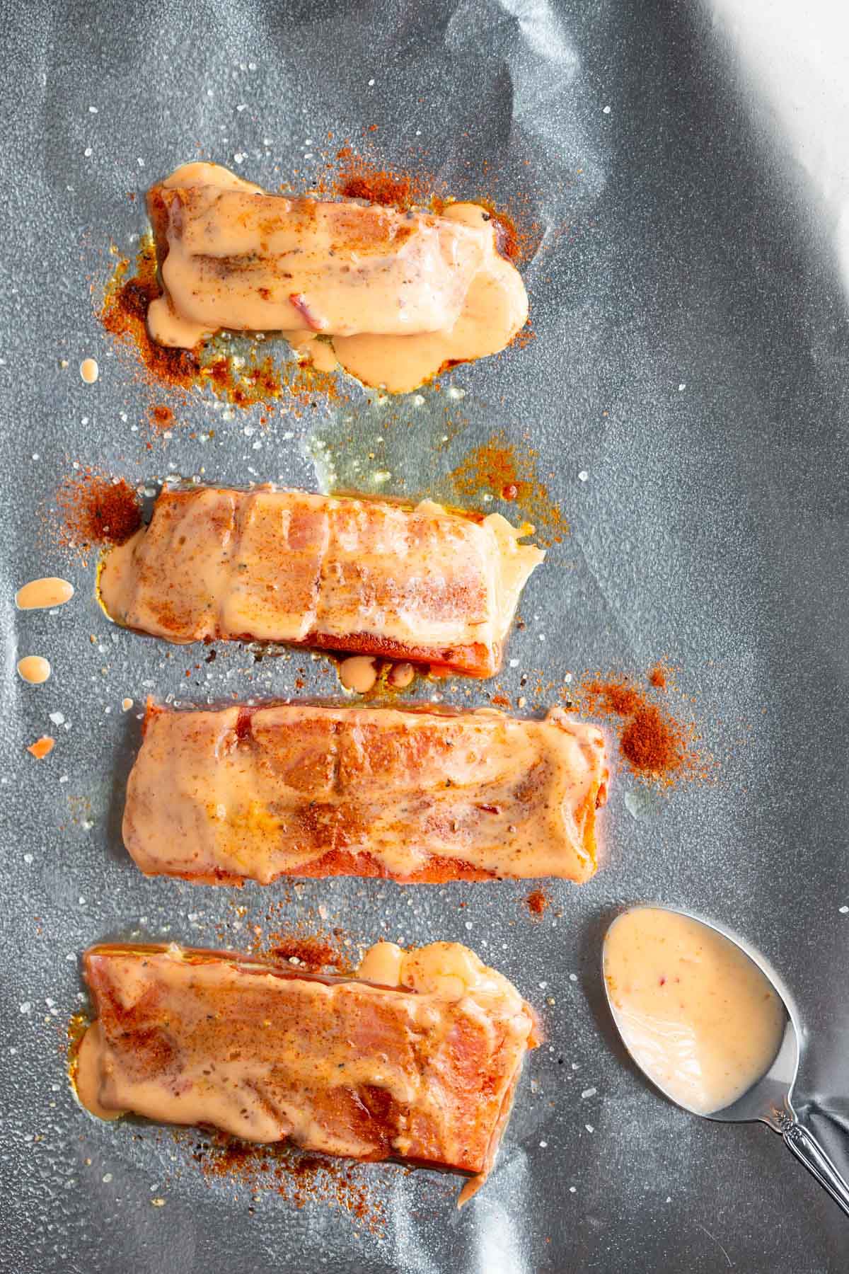 Salmon topped with bang bang sauce on a baking sheet.