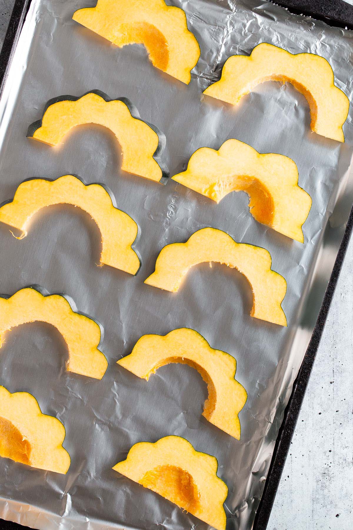 Uncooked acorn squash on a baking sheet.