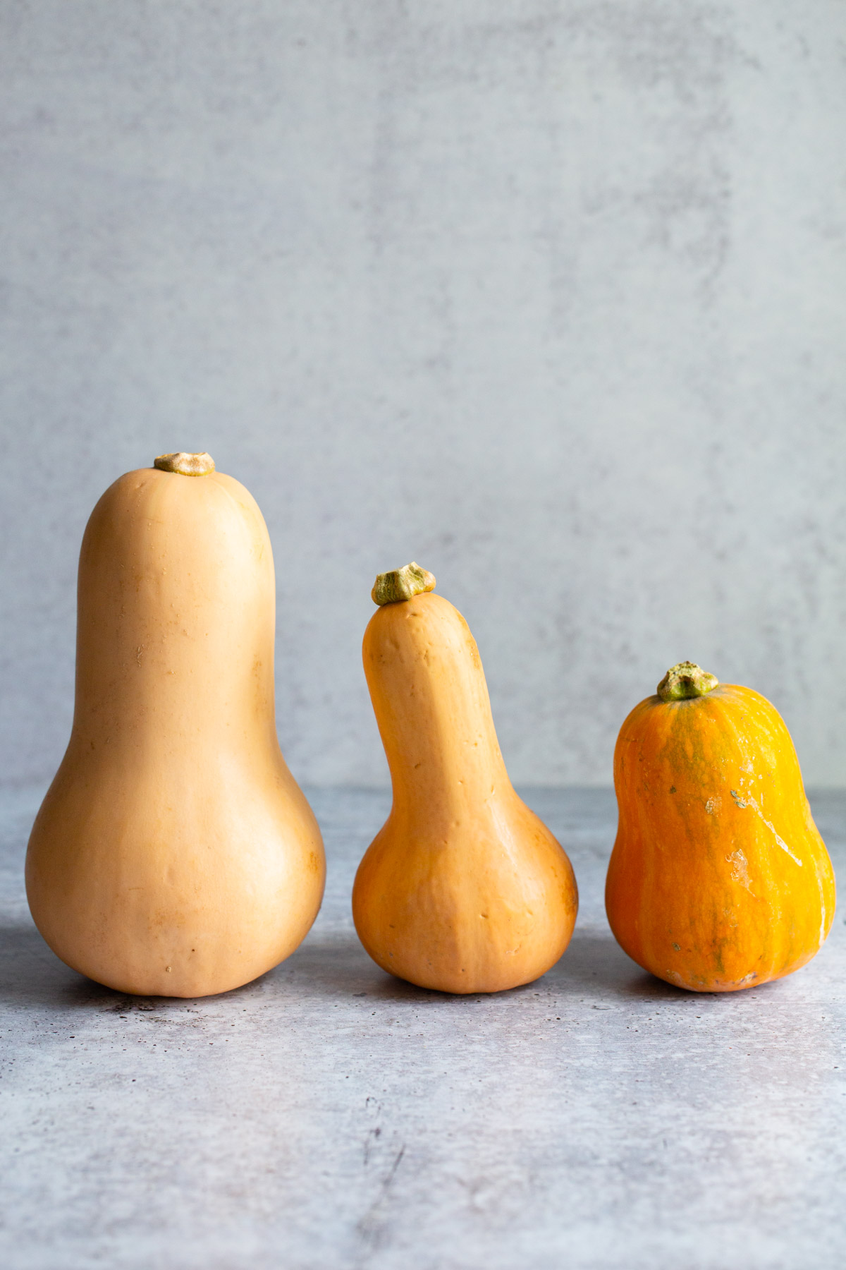 Butternut squash, honeypatch squash, and honeynut squash next to each other.